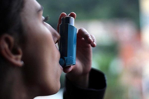 Junge Frau sprüht sich sich ein Asthma-Spray.