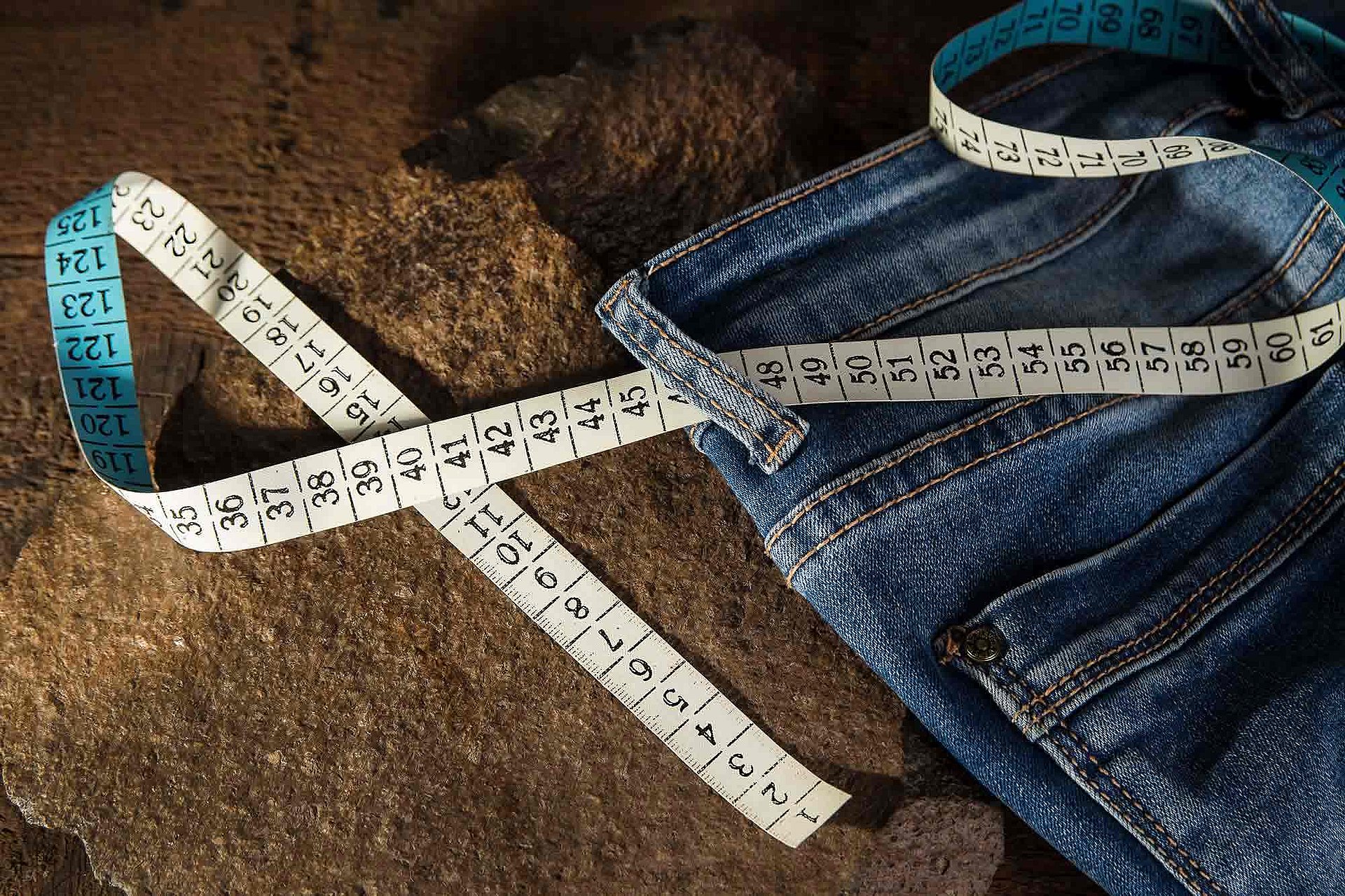 Zu sehen ist eine Bluejeans, durch die Gürtelschlaufen gezogen liegt ein Metermaß.
